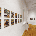 A view of a gallery space with white walls that shows colorful comic book covers on the walls.