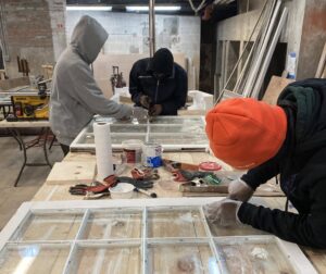 Two young men work on striping paint from old windows.