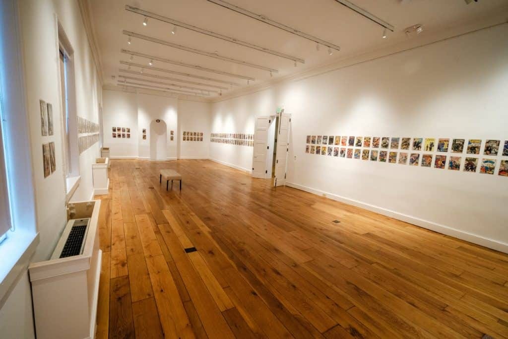A modern-looking gallery space with white walls and hundreds of small comic book covers on the walls.