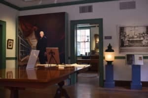 An interior room in a museum that features books on a table and a replica gaslight in the corner.