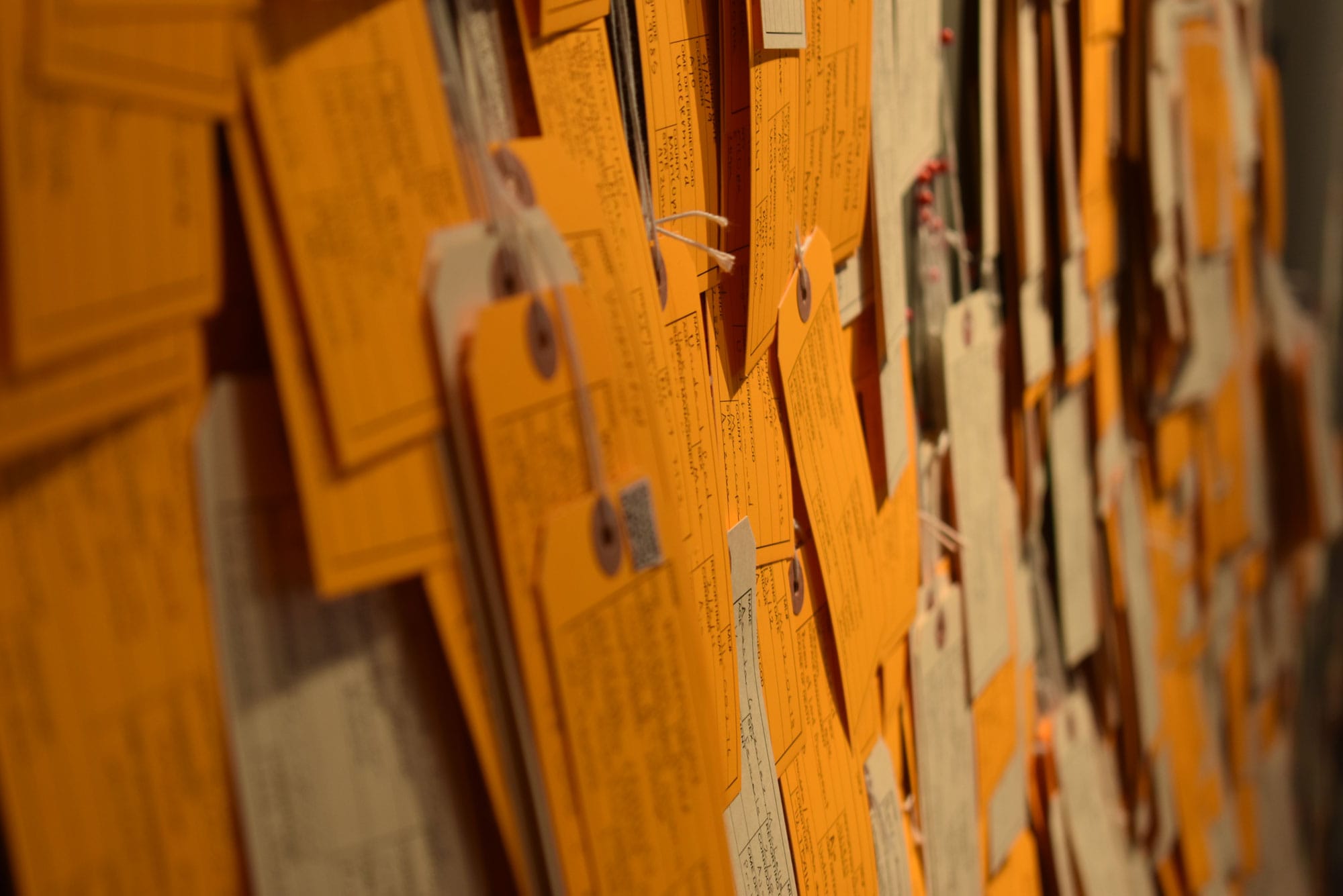 Dozens of yellow and white tags are displayed on a wall in a gallery.