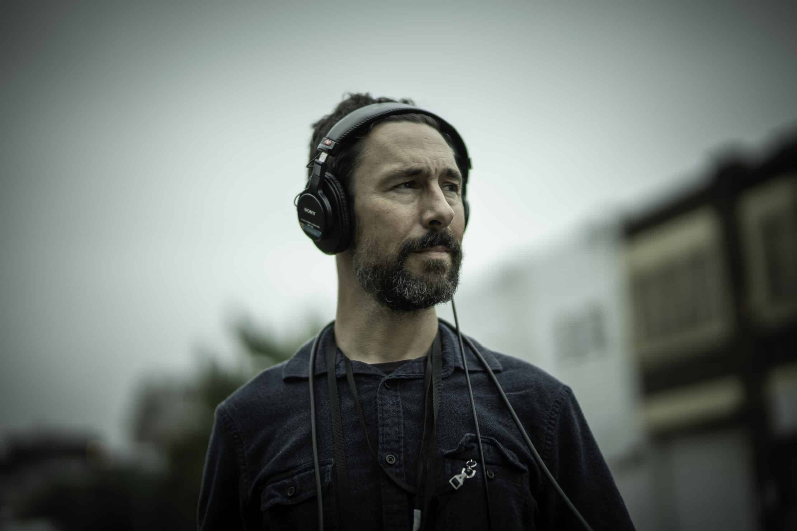 A man with a beard and headphones looks off into the distance.