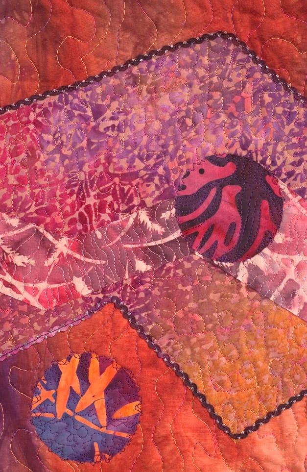 A close-up detail of a bright pink, purple, and blue quilt that shows batik patterns.