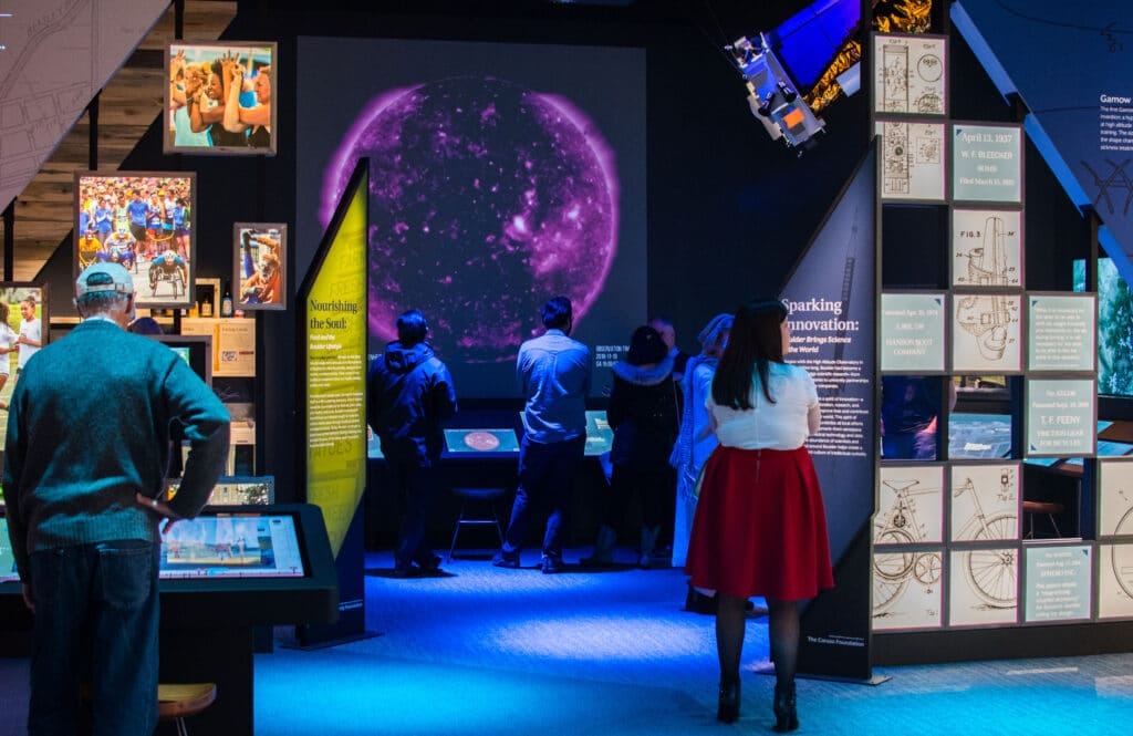 People stand in a dimly lit exhibition space that features outer space and planetary displays.