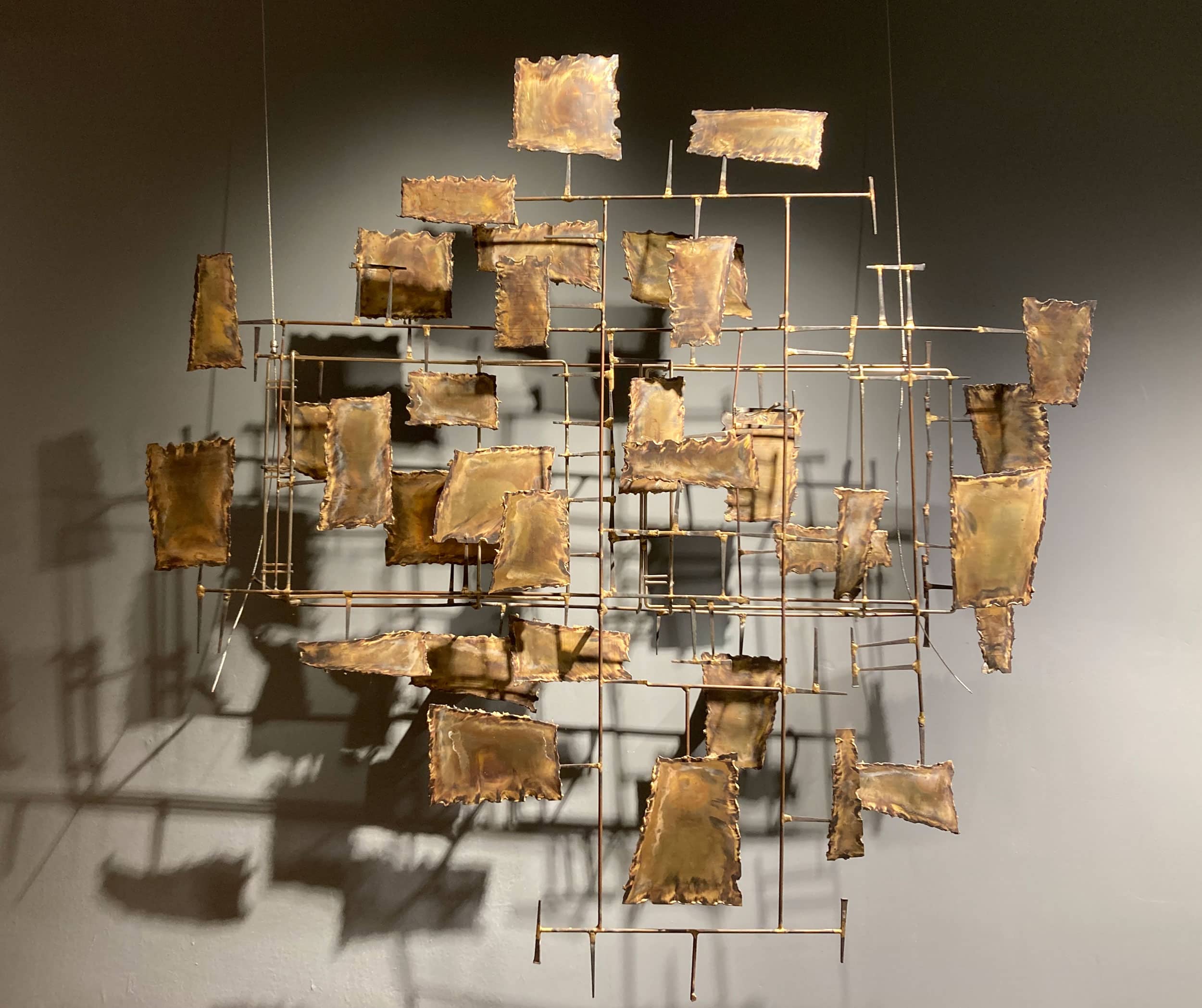 A metal sculpture that features gold squares mounted on long, thin bars.