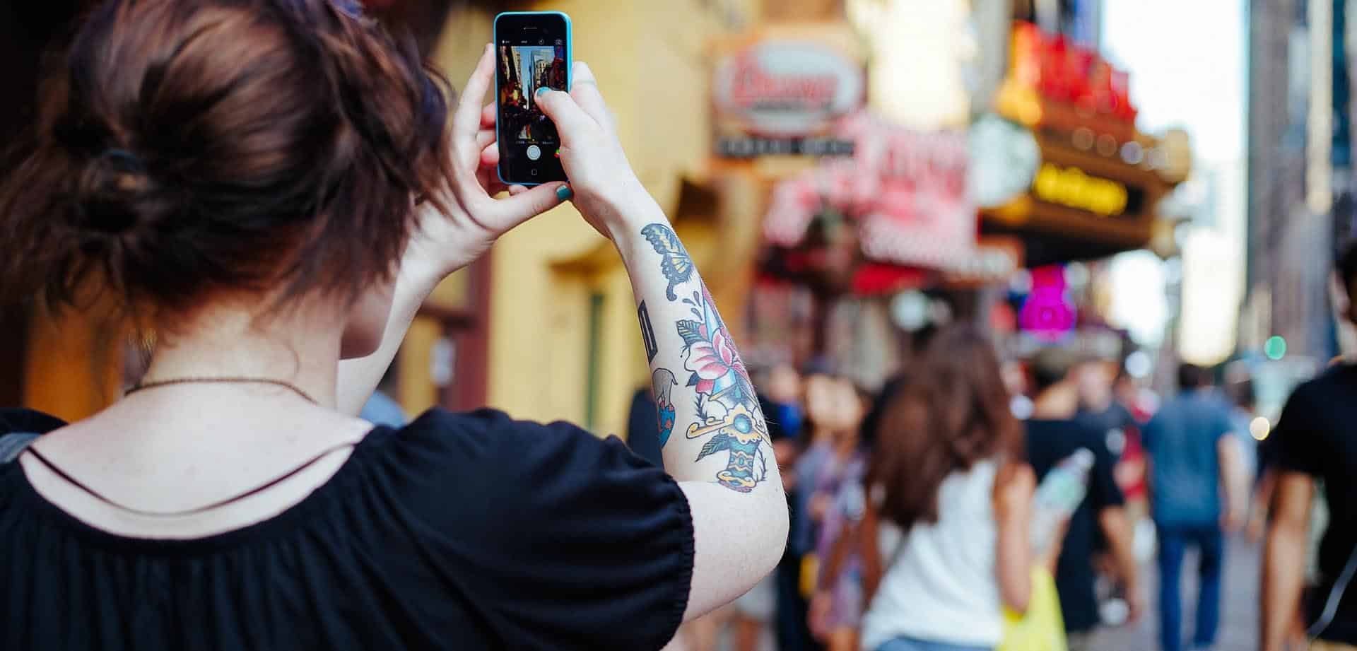 A person with a tattoo on her arm takes a picture of a building.