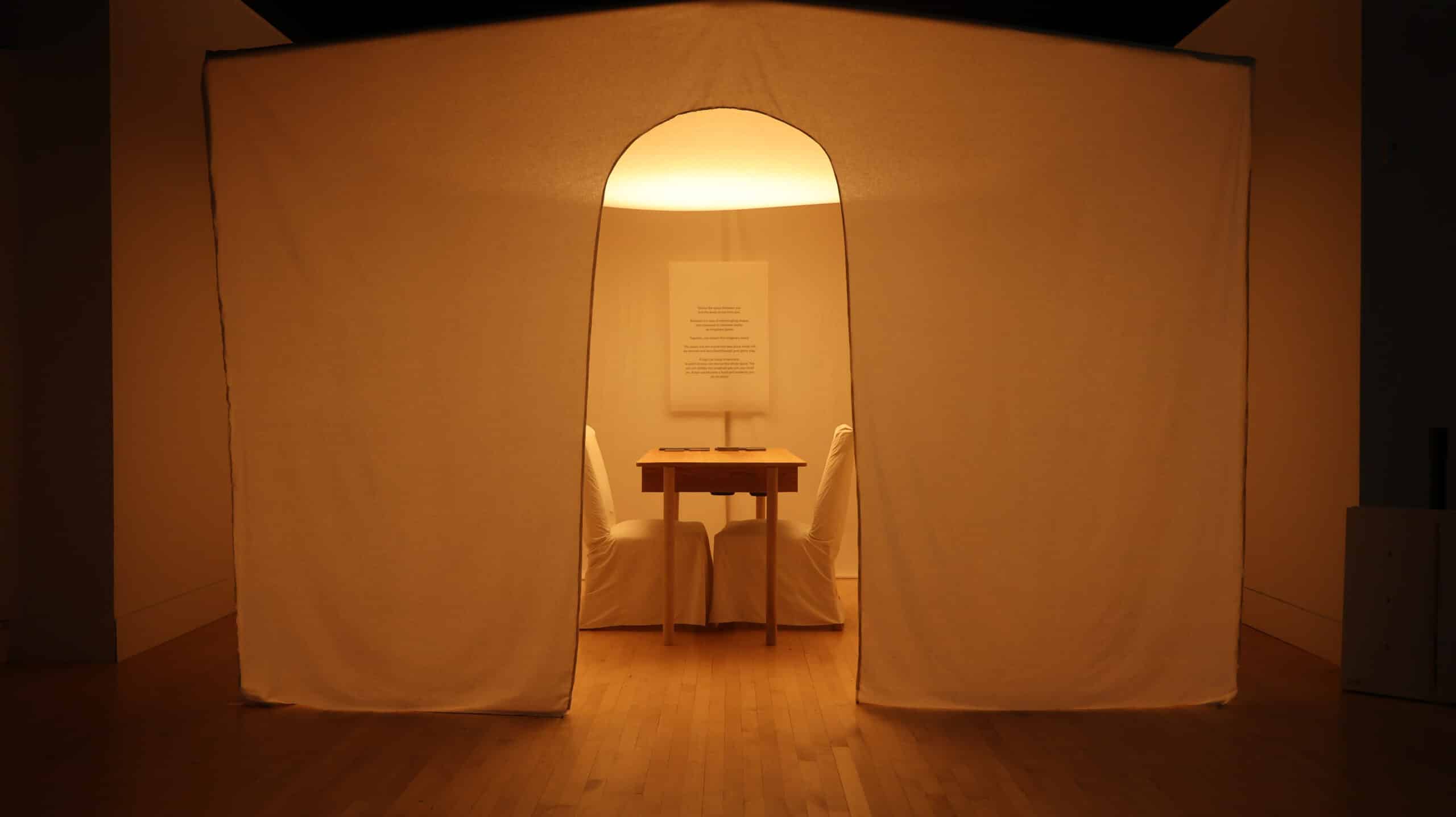 A tent inside a museum gallery that is bathed in warm light.