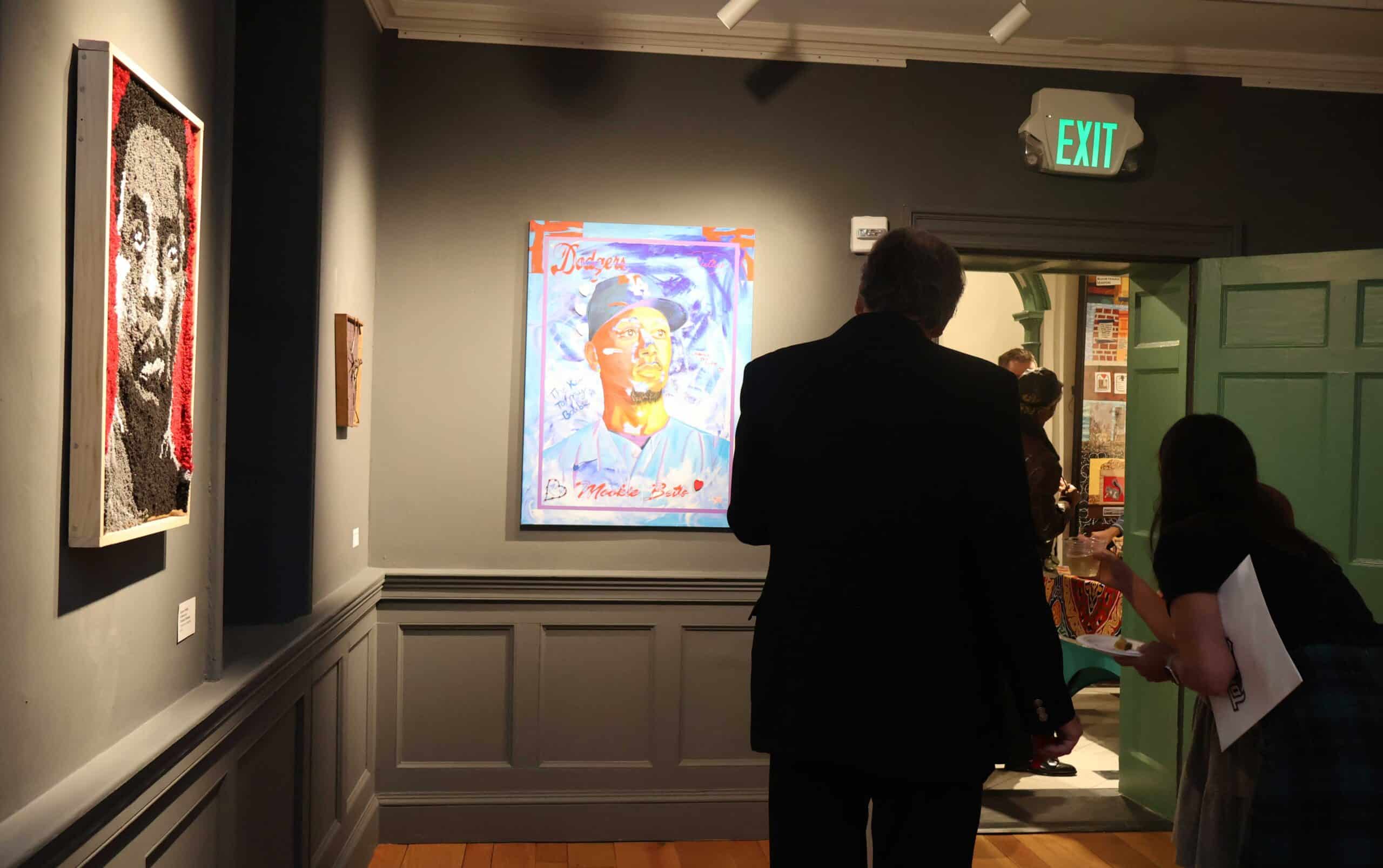 People stand around in a gallery and look at artwork that shows people's faces.