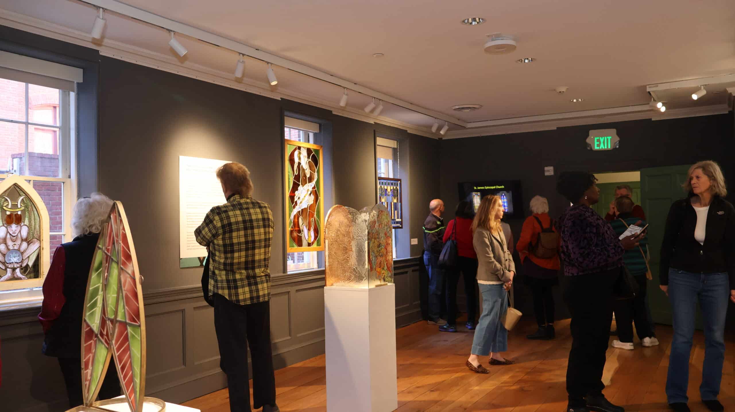 A group of people stand in a gallery that has stained glass items on display.