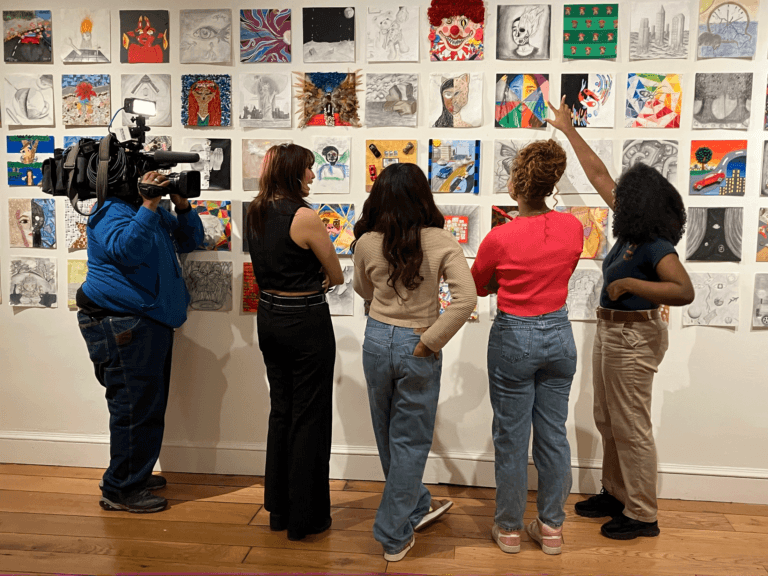 Three students talk with a reporter about their artwork in a gallery at The Peale.