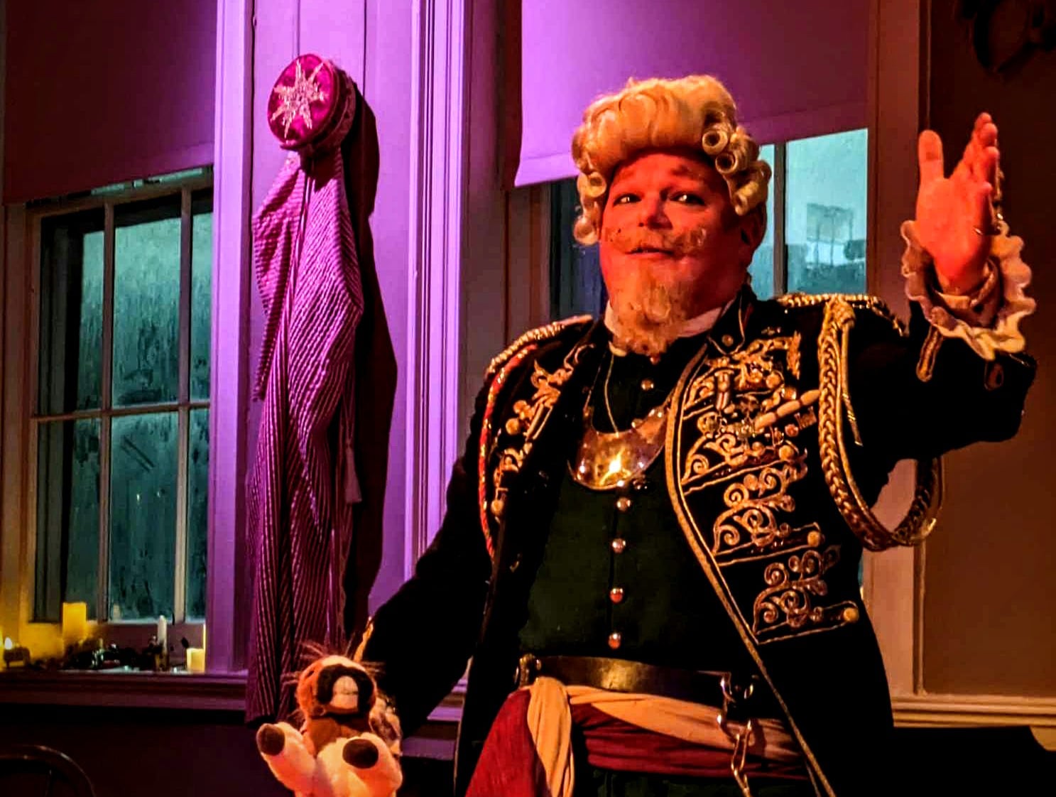 A man in a historic costume and a wig waves his hand welcoming visitors.