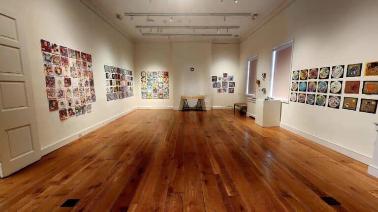 A gallery with wooden floors and small, quilt-like artworks on the walls.
