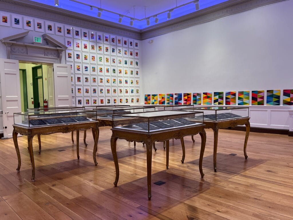 A gallery space with wooden cases and geometric artwork on the walls.