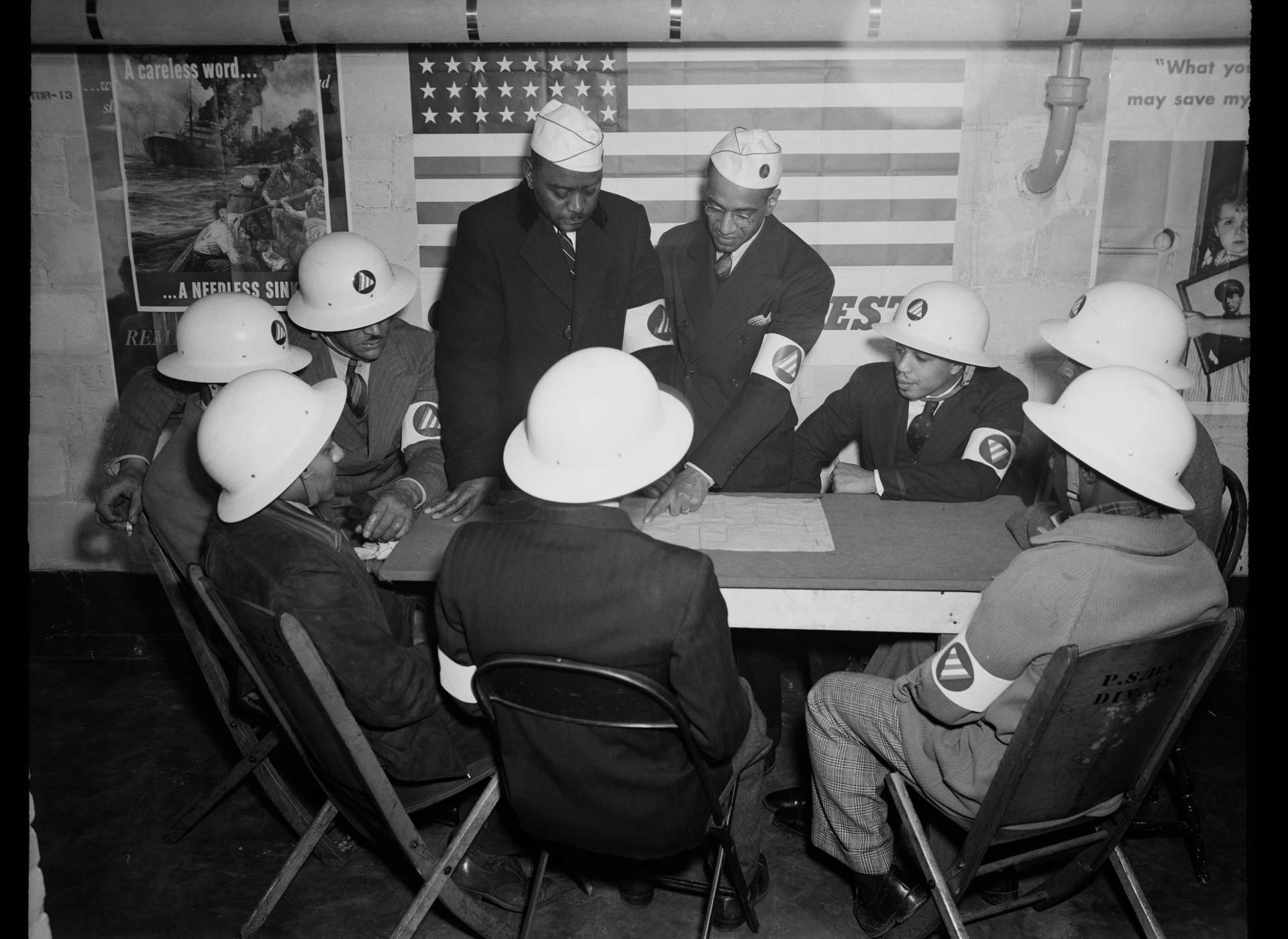 A group of African American men sit around a table. They work white hard hats in this vintage image.