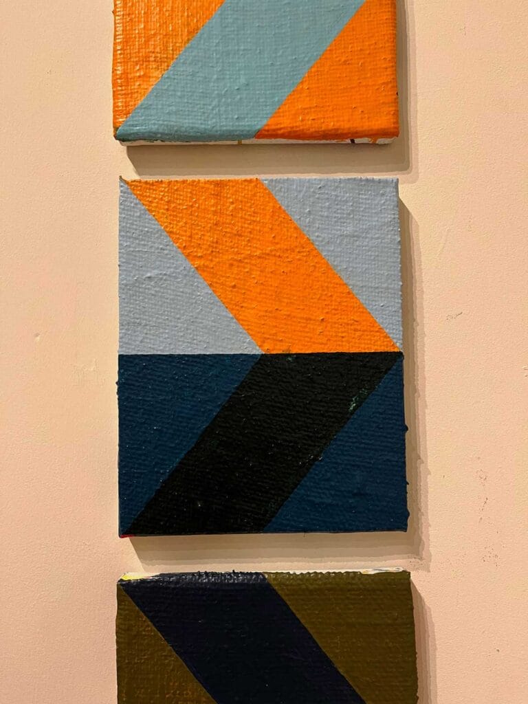 A series of paintings on a wall in a museum with orange and blue geometric shapes on canvas.