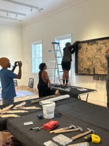 Three people install a quilt in a museum gallery.
