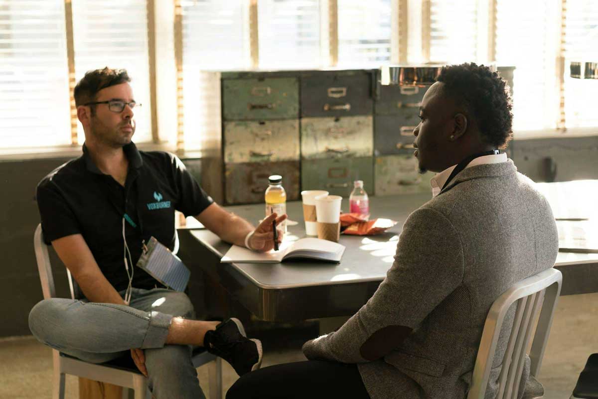 Two men sit in a coffee shop and talk.