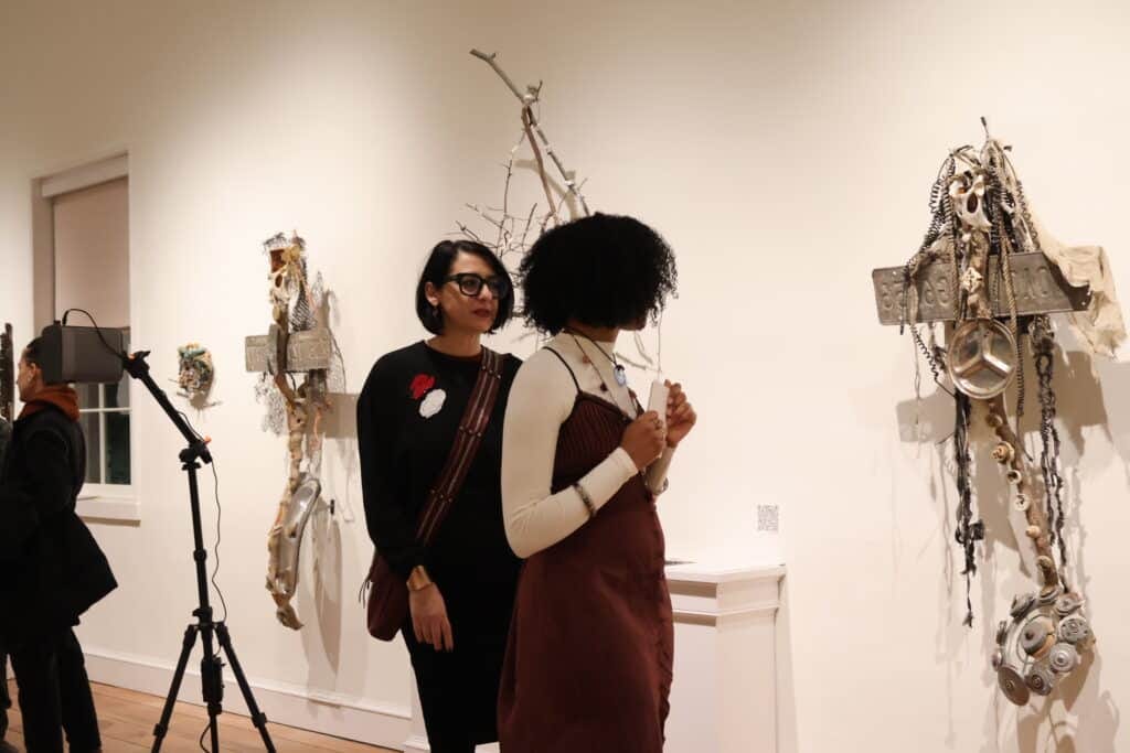 Two people walk through a gallery of art made from found, recycled objects.
