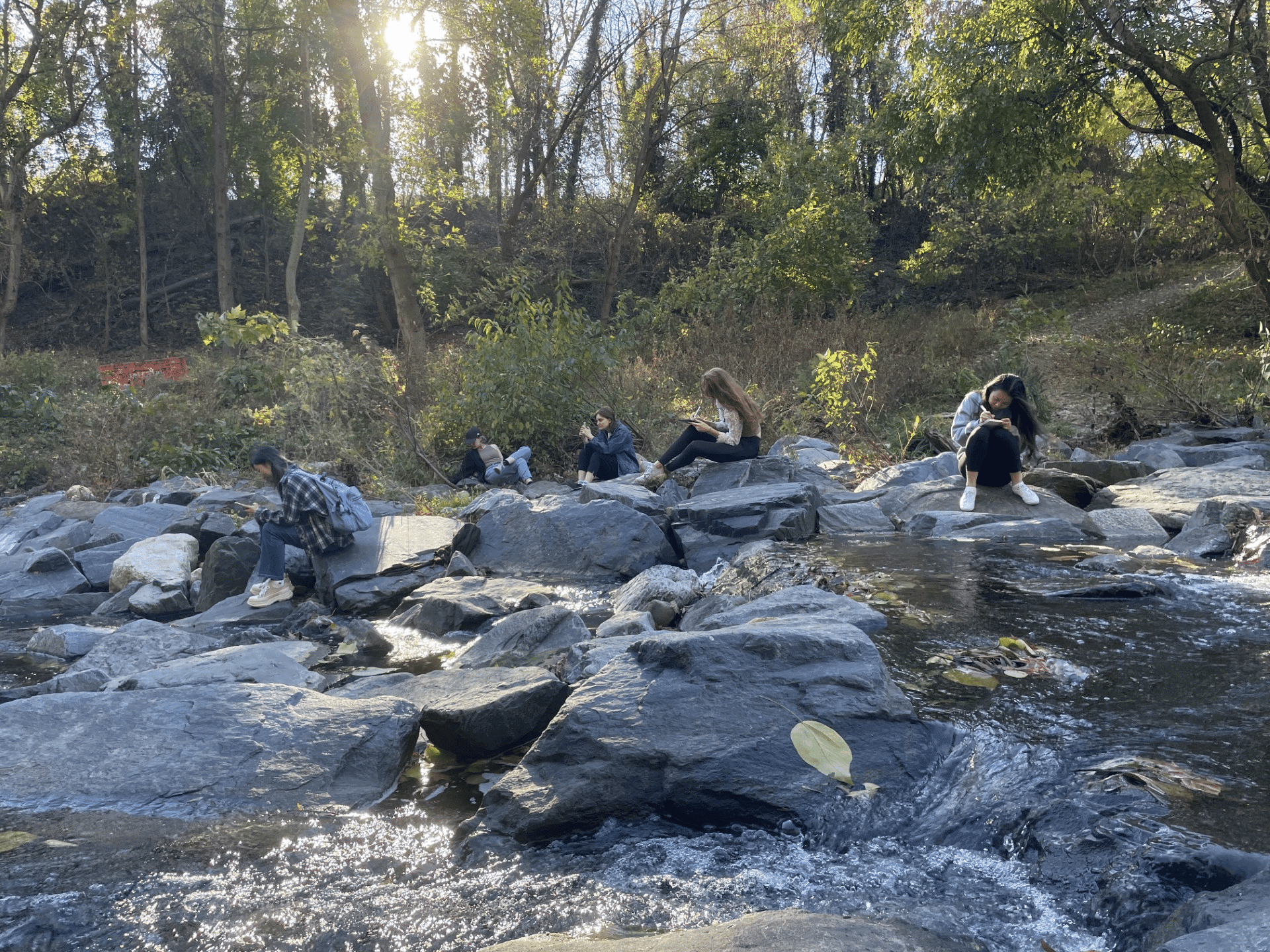 People sit on rocks in a river and write in journals.