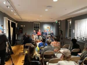 A room in a museum with dark gray walls filled with people in conversation.