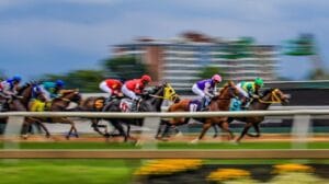 Horses carry jockeys in colorful shirts along a racetrack as the background blurs with speed.