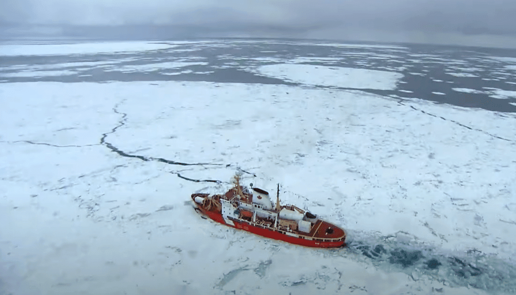 A vessel cuts through a path in a thick ice on the ocean.