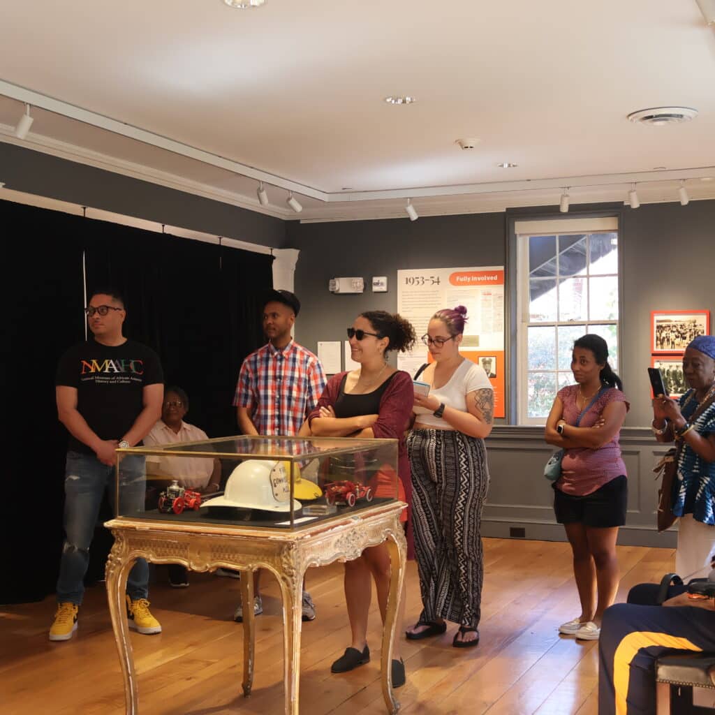 Group of visitors standing and looking at a glass display case on an ornate table in a museum gallery.