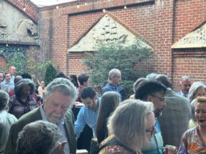 Crowd of people mingling at an outdoor event in a brick courtyard with string lights overhead.